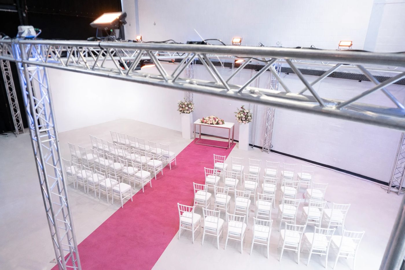 Ceremony in the studio with rows of chairs, a flower table and a pink carpet